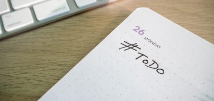 Close-up of a to-do list next to a computer keyboard on a desk.